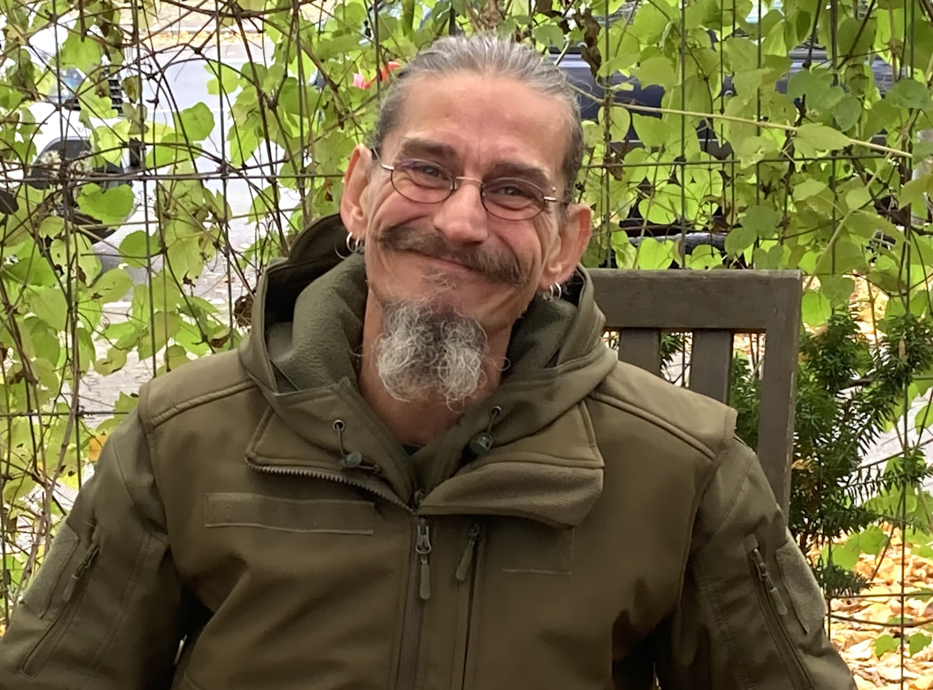 Jan von Jäger & Sammler auf einem Stuhl sitzender Mann mit Bart, runder, kleiner Brille mit einer kahkigrünen Jacke bekleidet.