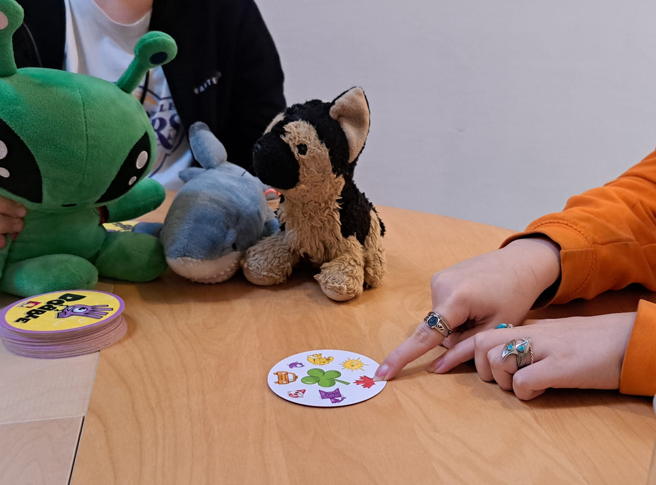 Eine Spielkarte liegt auf einem Tisch mit Stofftieren und zwei Hände deuten auf ein Symbol der Spielkarte.