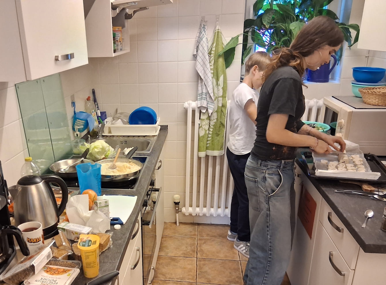 Junge Frau steht mit einem Kind in der Küche und kocht.