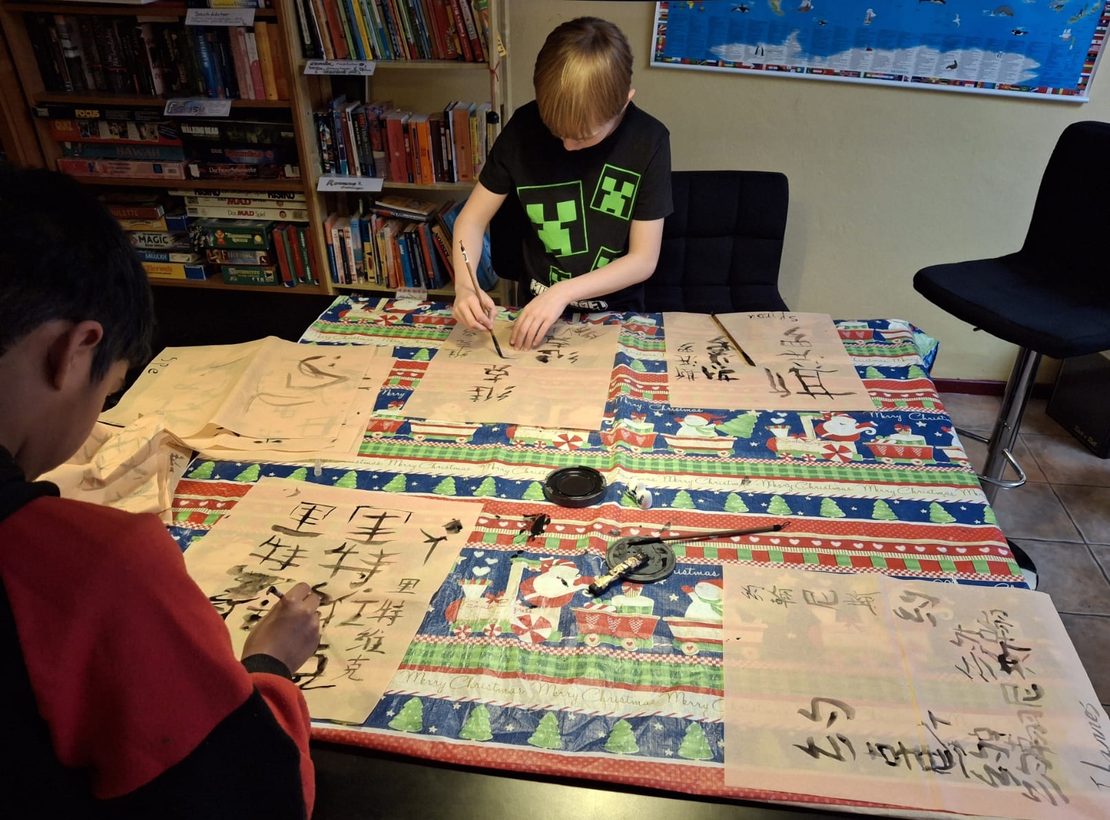 Zwei Kinder stehen an einem Tisch und malen chinesische Schriftzeichen.