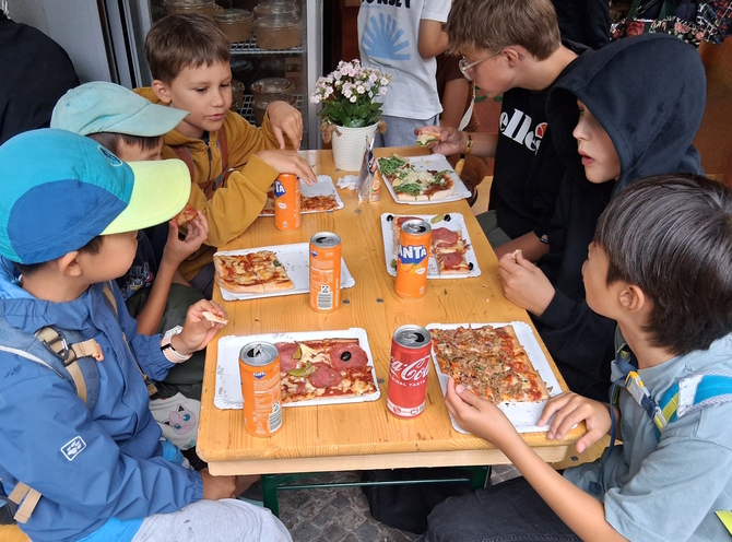 Kinder sitzen um einen Tisch und essen Pizza.