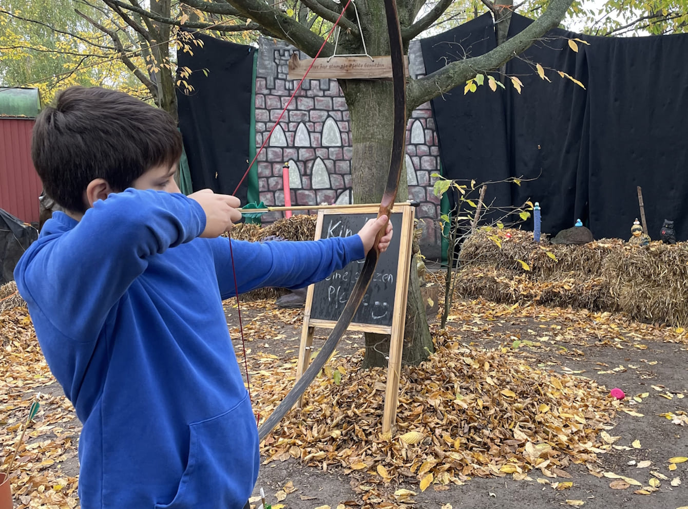 Junge im blauen Hoodie schießt mir Pfeil und Bogen auf ein Gummitier.