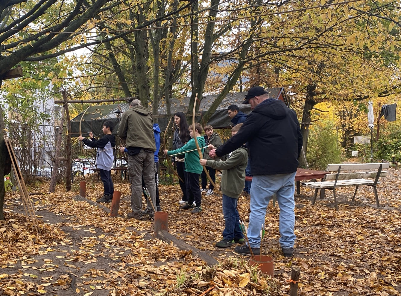 Gruppe von Kindern und Betreuern steht an einem Bogenschießstand mit Trainer im Herbst.