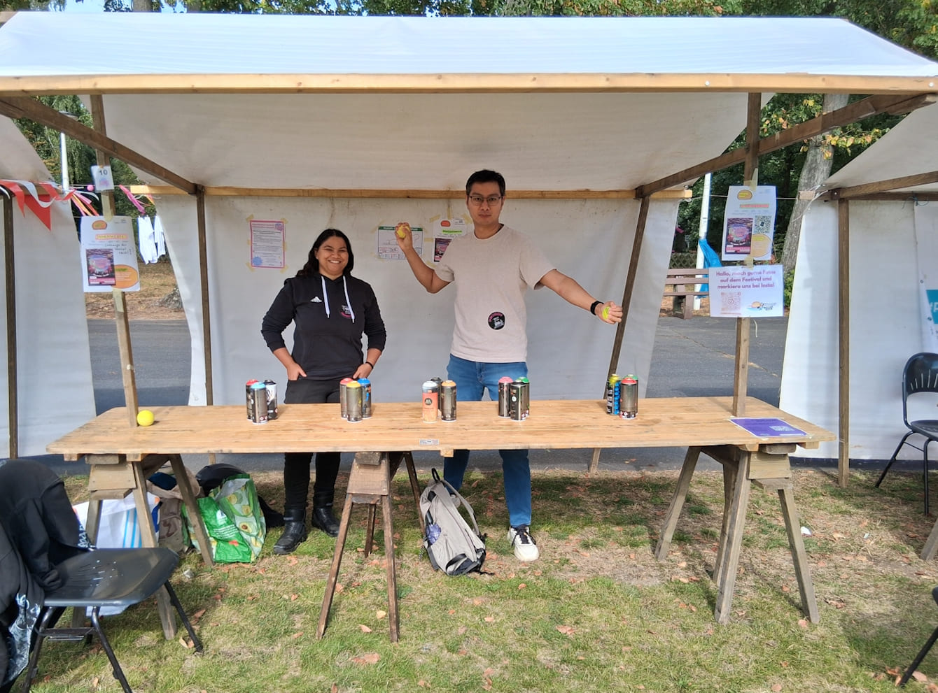 Zwei Mitarbeitende stehen hinter einem Stand, wo Dosenwerfen angeboten wird.