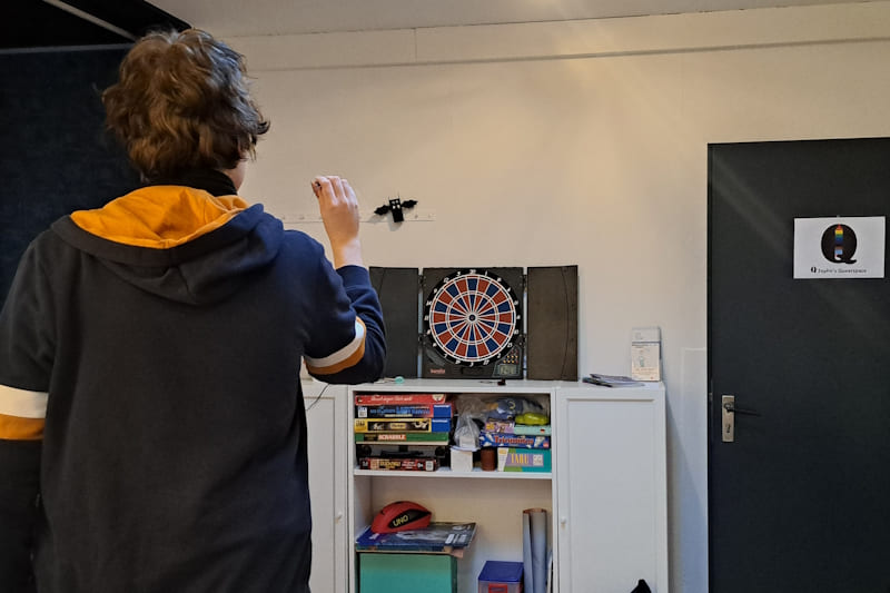 Eine Person, von hinten gezeigt, wirft einen Pfeil auf eine Dartscheibe.
