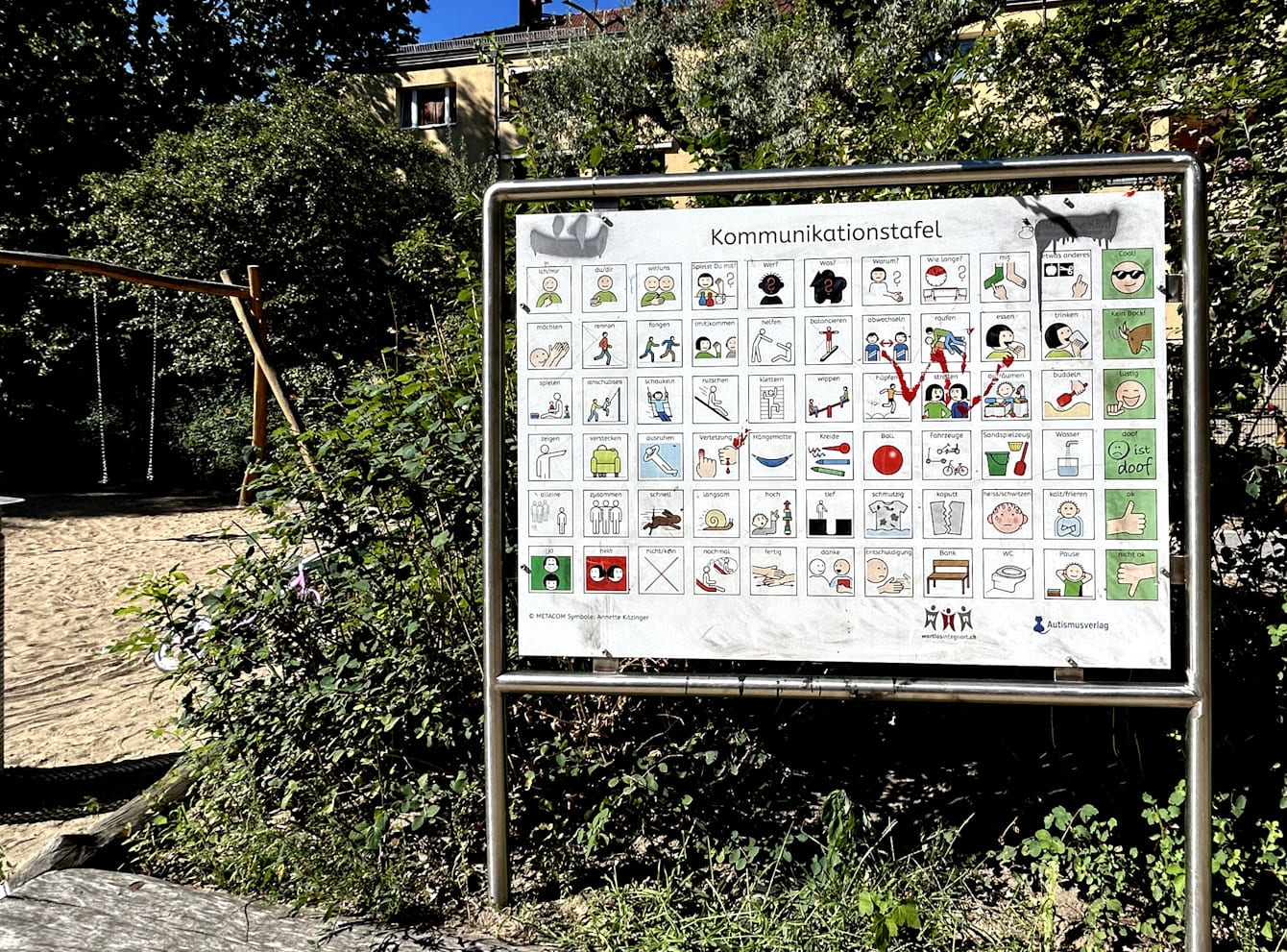 Komunikationstafel mit Pictogrammen für die "Unterstützten Kommunikation" am Rande eines Spielplatzes