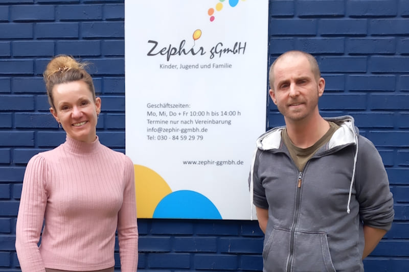 Eine Frau und ein Mann stehen vor dem Schild "Zephir gGmbH".