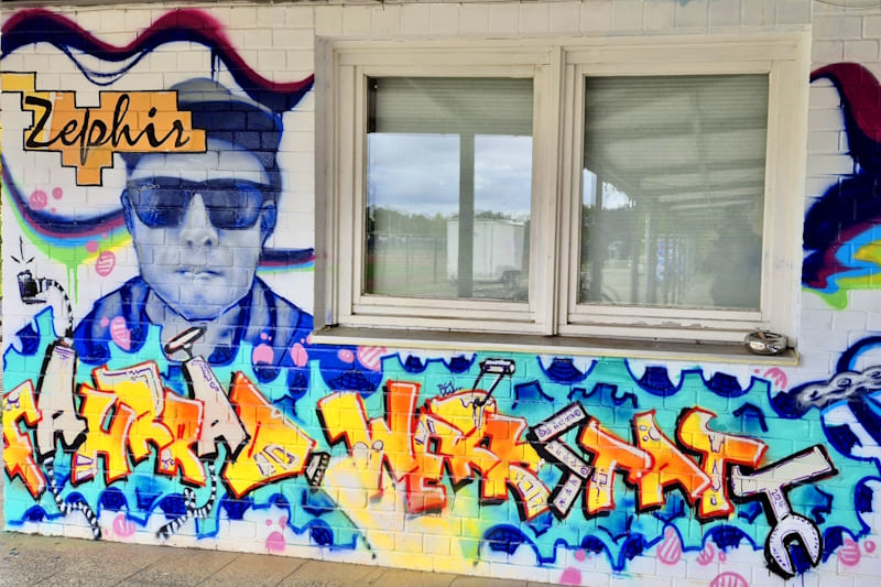 Graffiti an Hauswand mit Portrait und Piece "Fahrrad-Werkstatt"